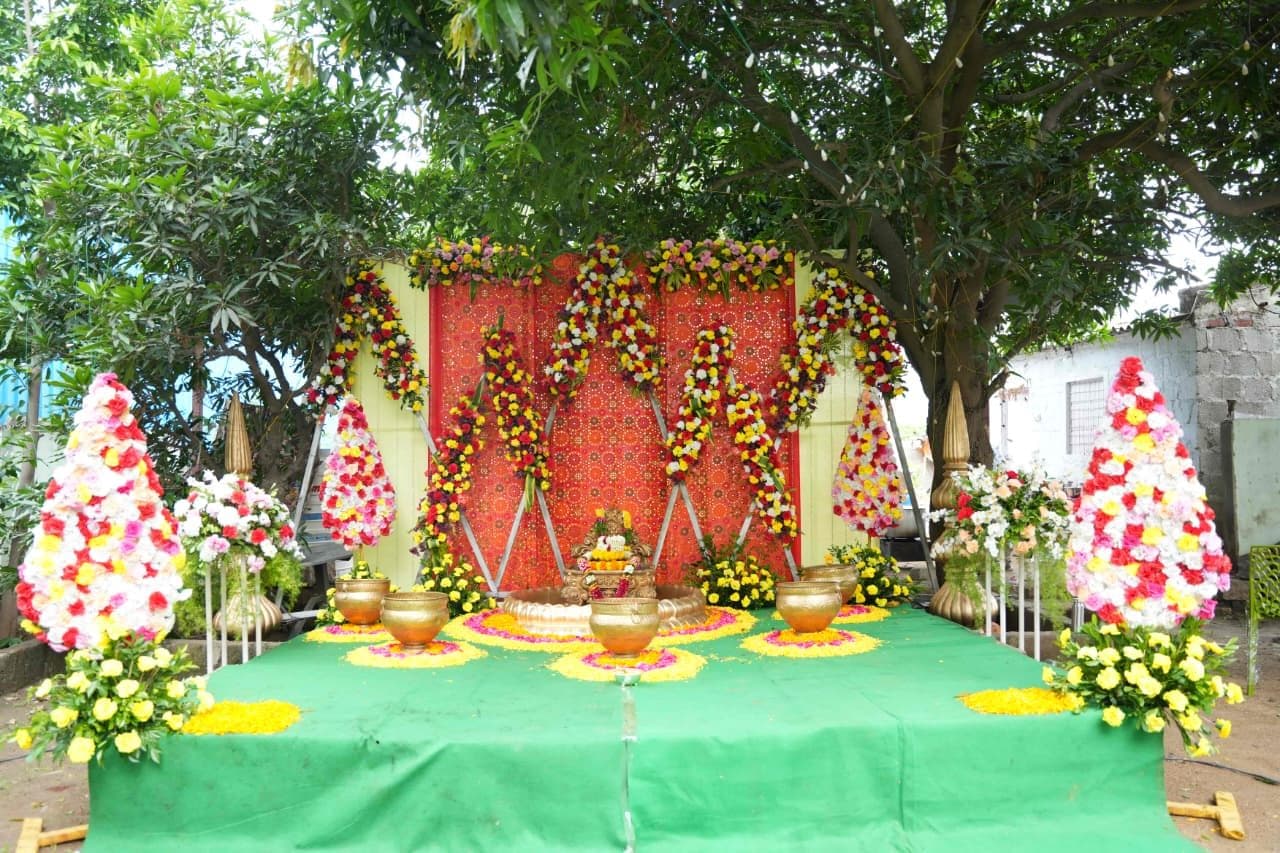 A traditional red and yellow floral mandap set beneath a tree